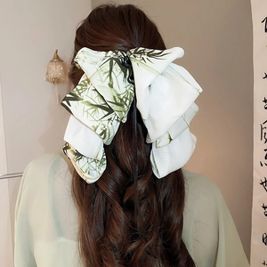 Detail of a large bow hair clip with green bamboo print worn on dark wavy hair