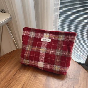 Détail macro d'une trousse à maquillage en laine à carreaux rouges sur table en bois