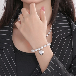 Gros plan d'un bracelet en perles blanches orné d'un pendentif en forme de cœur argenté