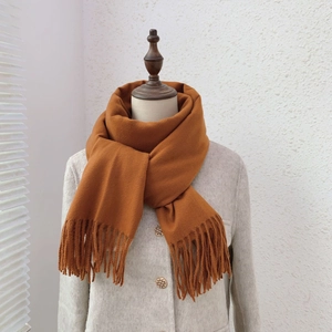 Close-up of a soft caramel solid color scarf with tassel details on a mannequin neck