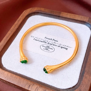 Detailed close-up of vintage gold bangle with green emerald-like stones and zircon accents