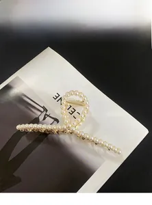 Détail d'une grande pince à cheveux en métal doré avec perles blanches sur fond noir
