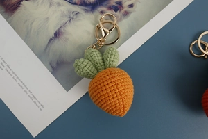 Handmade crochet carrot keychain with orange yarn body and green leaves on blue background