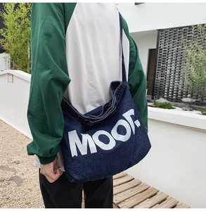 Detail of deep blue denim tote bag with large white MOO letters shown on model