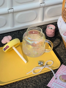 Detail view of cloud glass mug with rainbow spots and pink mushroom lid in a picnic setup