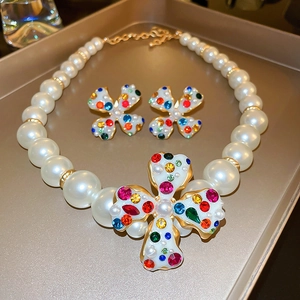 Three-piece jewelry set with pearl necklace and flower earrings on a golden tray