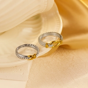 Two-tone woven stainless steel rings with gold knots on white ceramic base