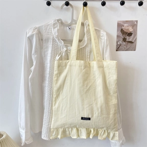 Detail of cream canvas tote bag featuring vertical textures and a bottom ruffle edge