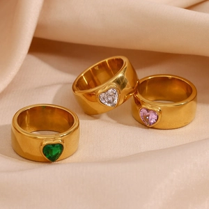 Three gold-plated rings with colorful heart-shaped stones on beige silk fabric background