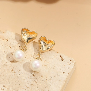 Macro view of gold heart frame and round pearl pendant on a beige stone surface