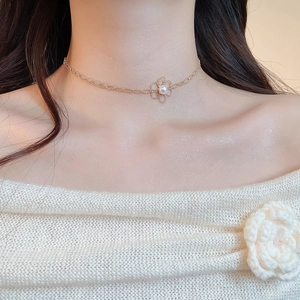 Close-up of a delicate gold flower pendant necklace with pearl center worn on neck