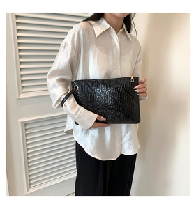 Detail of a black croc-embossed envelope clutch with gold zipper and wrist strap