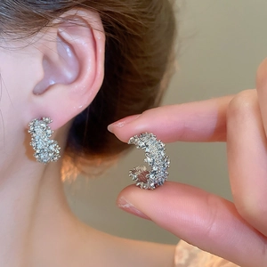 Détail de boucles d'oreilles argentées en C avec une texture métallique froissée