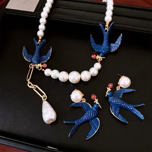 Elegant pearl jewelry set with blue enamel swallows and red rose charms on black leather