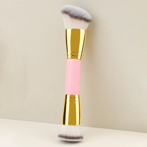 Close-up of dual-ended makeup brush with pink handle and golden ferrules on beige base