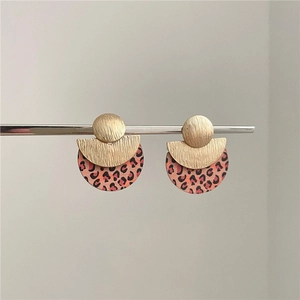 Golden geometric earrings with leopard print circles on a minimalist grey background