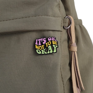 Enamel dopamine badge brooch with 'IT'S OK NOT TO BE OKAY' quote on a backpack