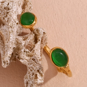 Close-up of gold stainless steel bangle with green gemstones on white rock