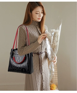 Detail of black pebbled leather tote with embossed letters and red contrast handle