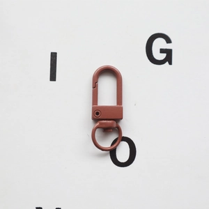 Macro view of a reddish-brown lacquered metal swivel lobster clasp with a D-ring and hook
