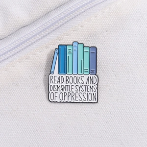 Enamel book brooch featuring colorful books and Read Books Dismantle Systems text on canvas