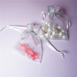 Detailed view of white organza drawstring gift bag with silver ribbon bow and pearls