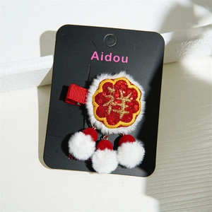 Detail of red festive hair clip with embroidery, white plush trim and dangling pom-poms