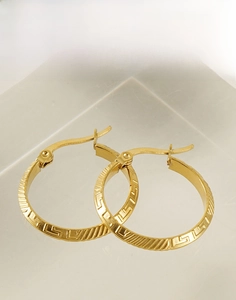 Close-up of golden stainless steel hoop earrings with engraved geometric texture