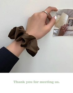 Close-up of silky dark brown satin scrunchie on wrist with vintage art backdrop