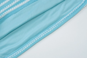 Detail of light blue fabric with white lace embroidery and fine sewing stitch work