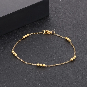Detail of a minimalist gold beaded chain bracelet with lobster clasp on a black surface