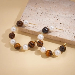 Detailed view of C-shaped earrings with alternating tiger eye stones and white pearls