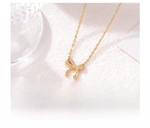 Close-up of golden bow pendant necklace with micro-pave crystals on white fabric