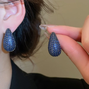 Detailed view of silver needle teardrop earrings with pavé blue zircons in black metal
