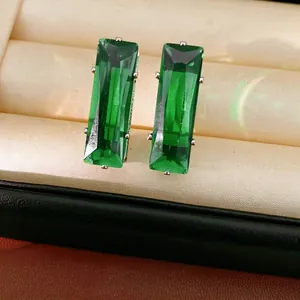 Elegant emerald green rectangular drop earrings set in silver claws inside a jewelry box