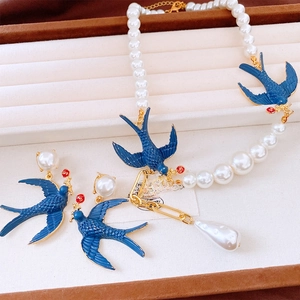 Detail view of pearl necklace and swallow earrings set on a velvet jewelry tray