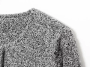 Gros plan sur la texture bouclée grise et le bouton doré d'une veste élégante