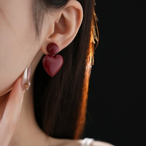 Close-up of model wearing burgundy heart-shaped dangle earrings with a glossy finish