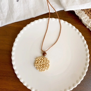 Bohemian wax cord necklace with handmade beaded round pendant on a ceramic dish