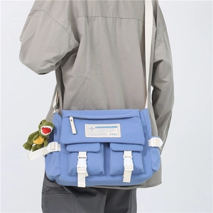 Blue Japanese retro messenger bag with green dinosaur pendant worn by model in a side view