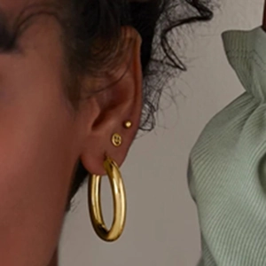 Close-up of golden hoop earrings and a mini smiley face stud worn on the earlobe