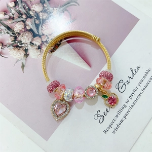 Close-up of gold beaded bracelet with pink heart and cherry charms on a floral card