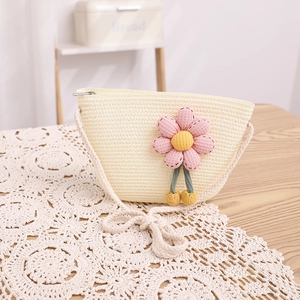 Détail d'un sac bandoulière en paille beige avec des fleurs décoratives sur dentelle