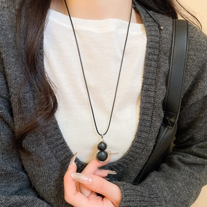 Close-up of black gourd pendant with silver edges on a long sweater chain