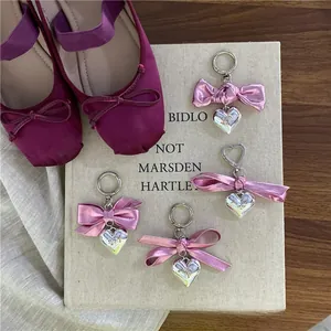 Close-up of four silver heart charms with shiny pink bows on a beige display board