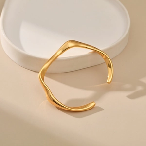 Detalle de un brazalete abierto dorado minimalista con líneas curvas irregulares