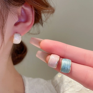 Close-up of pastel C-shaped stud earrings in pearl white and pink on a female model