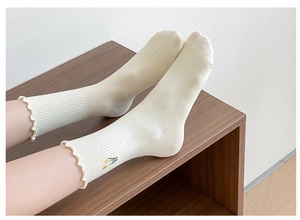 Close-up detail of women's beige mid-tube socks featuring cute floral embroidery and ruffles.