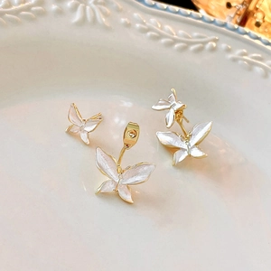 Detailed view of gold butterfly stud earrings with white pearl enamel on a white plate