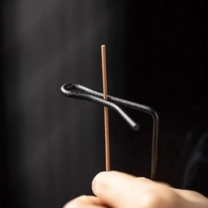 Minimalist black metal hanging incense burner with brown stick held in a hand